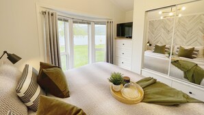 Un dormitorio con cama, una mesita de noche con una planta, un espejo y vistas al exterior a través de la ventana.