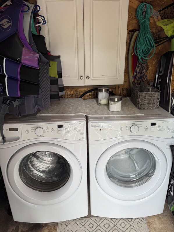 Dos lavadoras Whirlpool de carga frontal, un armario blanco con etiquetas y una cesta de mimbre sobre un piso de baldosas.