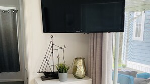 Una sala de estar con un televisor de pantalla plana sobre un mueble blanco, una planta en maceta y un jarrón decorativo.