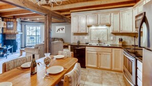 Une cuisine spacieuse avec des meubles de rangement en bois, un coin repas doté d’une table en bois et un lustre.