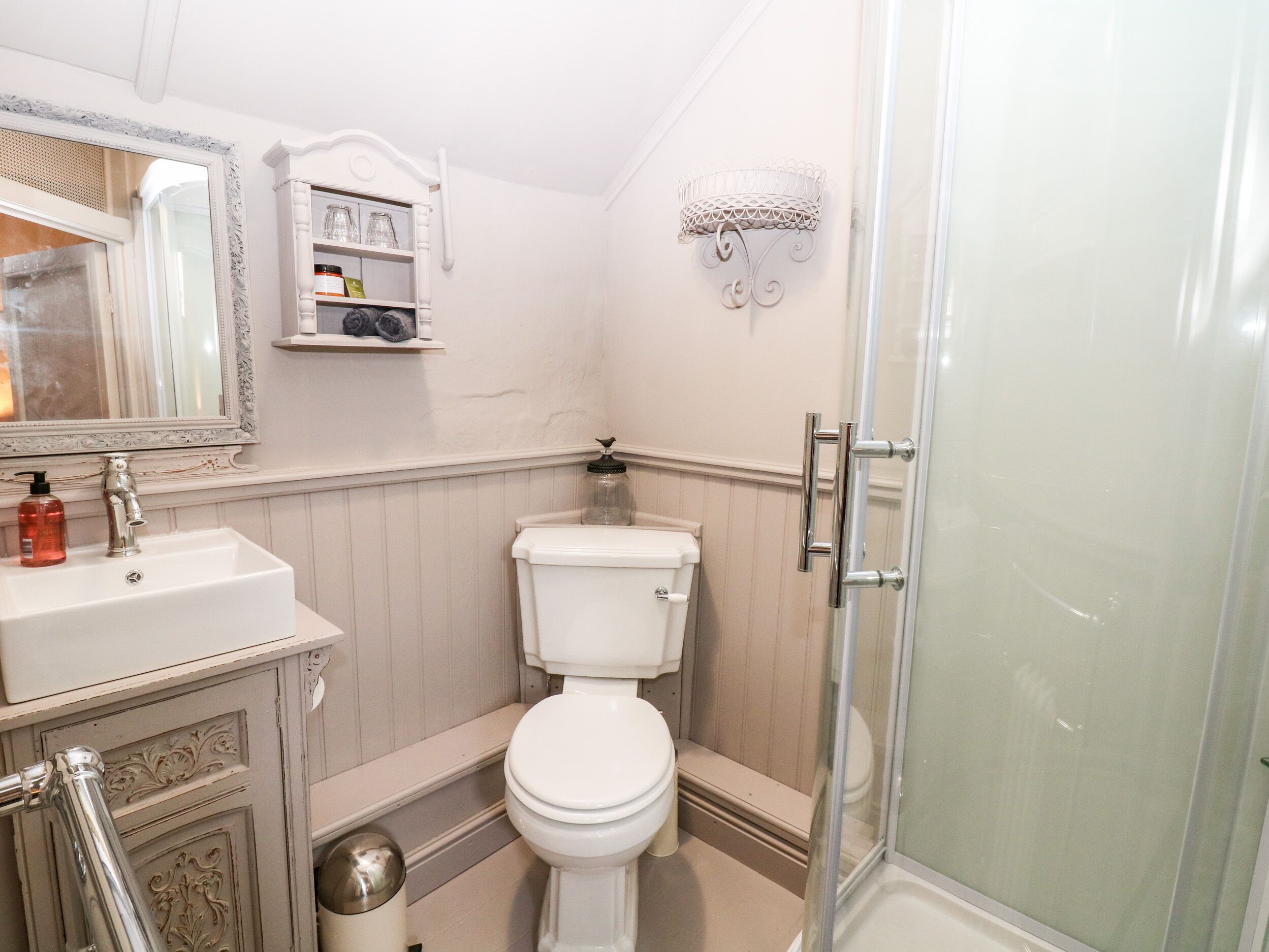 A bathroom with a white sink, a toilet, a glass shower enclosure, and a mirror with a decorative frame.