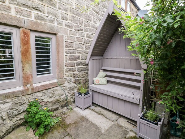 A stone building with a window, a wooden bench, and potted plants. - The Mouse House (Matlock)