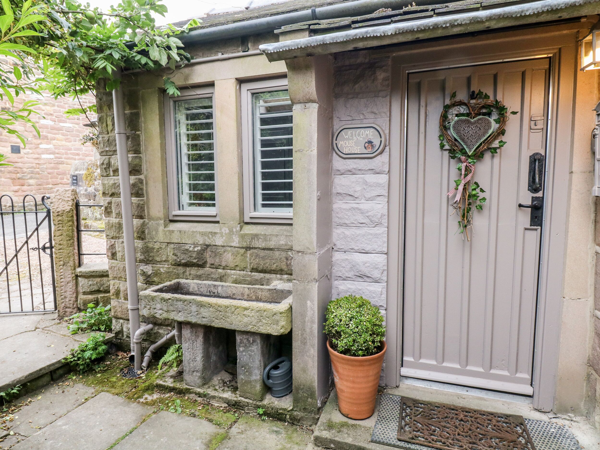 A stone house with a grey door, a heart-shaped decoration, and a welcome sign.