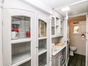 A bathroom with a toilet, a sink, and a mirror. There is a window with a curtain and a shelf with a red pot and a white pitcher.