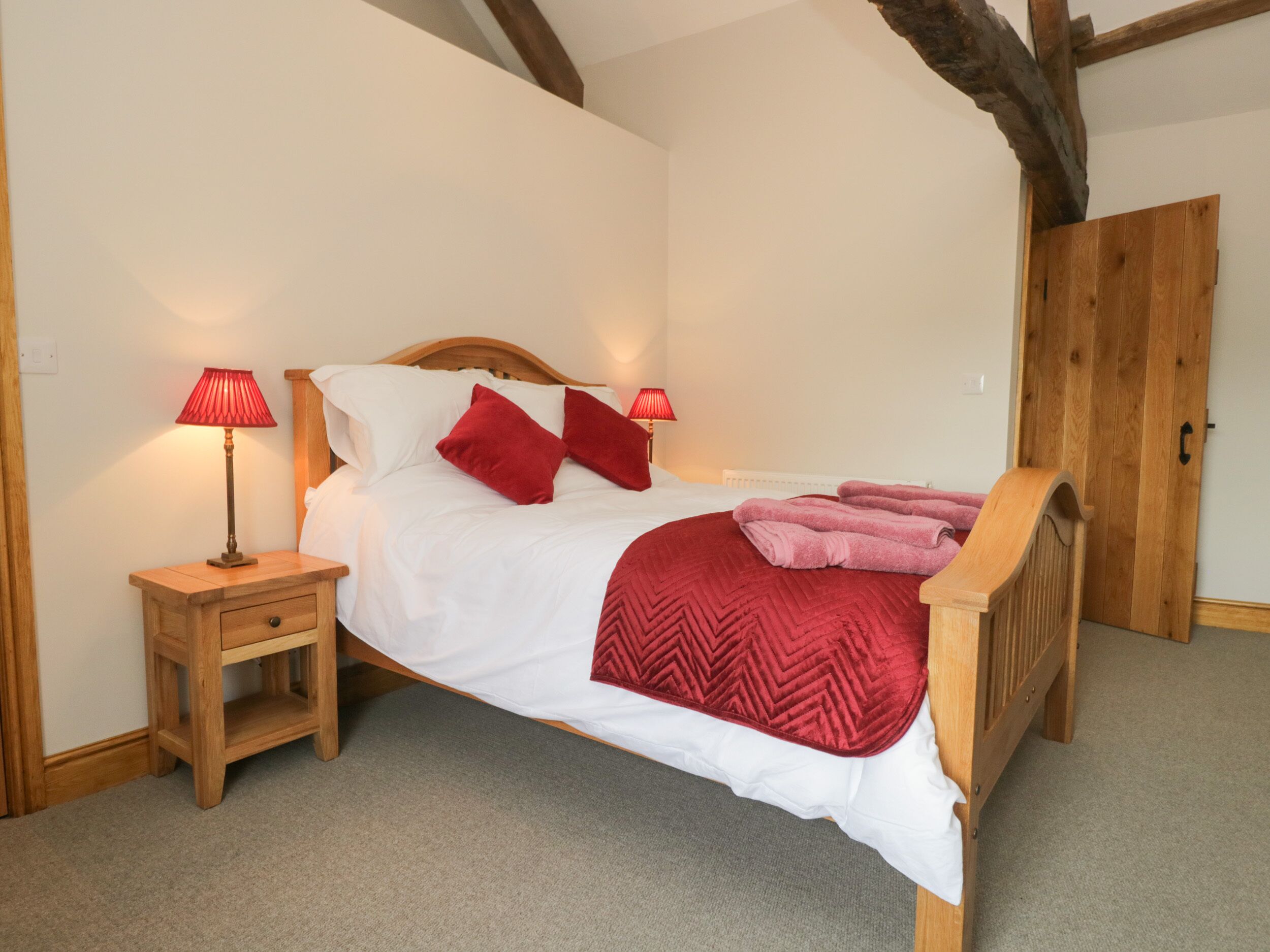 A neatly made bed with a wooden headboard, two bedside tables with lamps, and a wooden wardrobe.