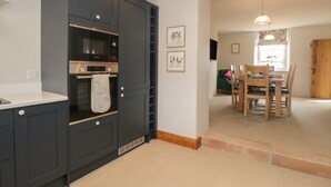 A modern kitchen with built-in appliances, a dining area with wooden furniture, and a view of the outside through a window.