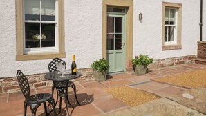 A building with a white exterior, a green door, and a small patio area with a table and chairs.