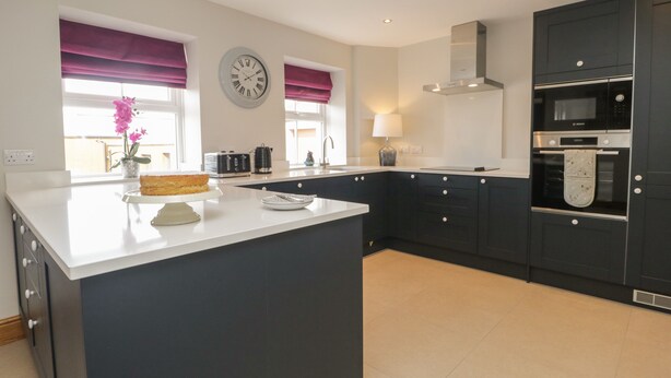 A modern kitchen with a central island, dark cabinetry, and a clock on the wall.