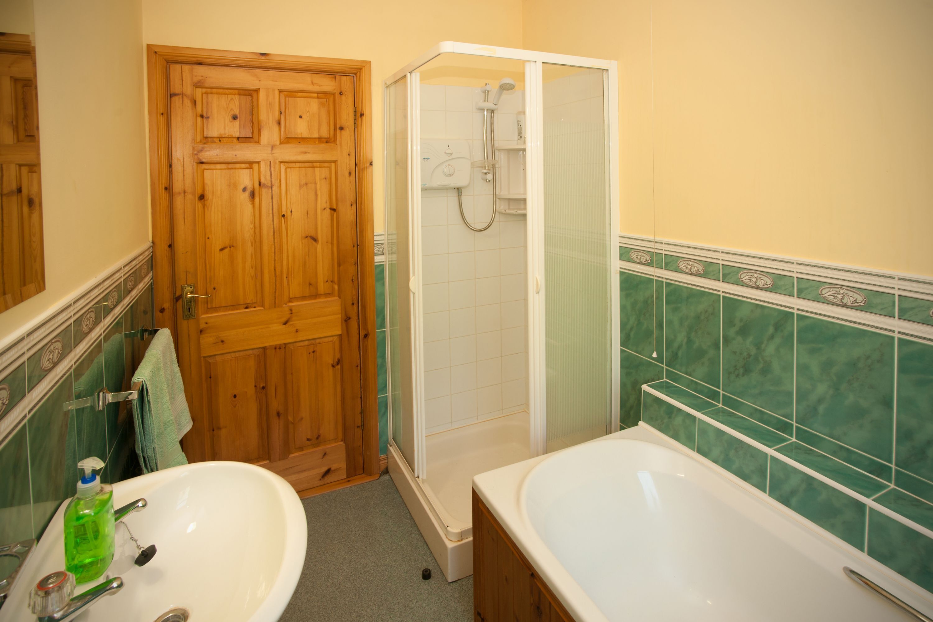 Un baño con puerta de madera, cabina de ducha, lavabo con una botella verde y bañera.