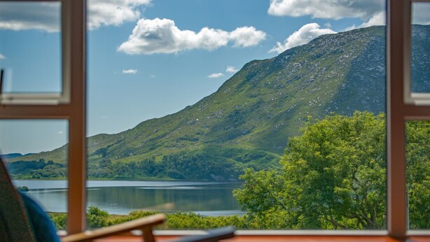 A view from a window of a room with a chair, a lake, and a mountain.