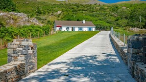 A house with a stone wall on one side and a paved driveway leading to it.