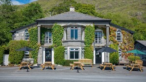 A stone building with ivy-covered walls, wooden benches, and tables in front.