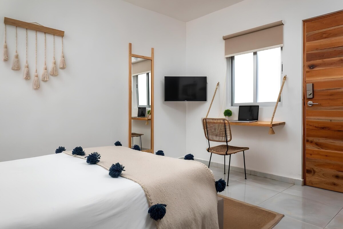 A modern bedroom with a bed, a TV, a chair, and a window.