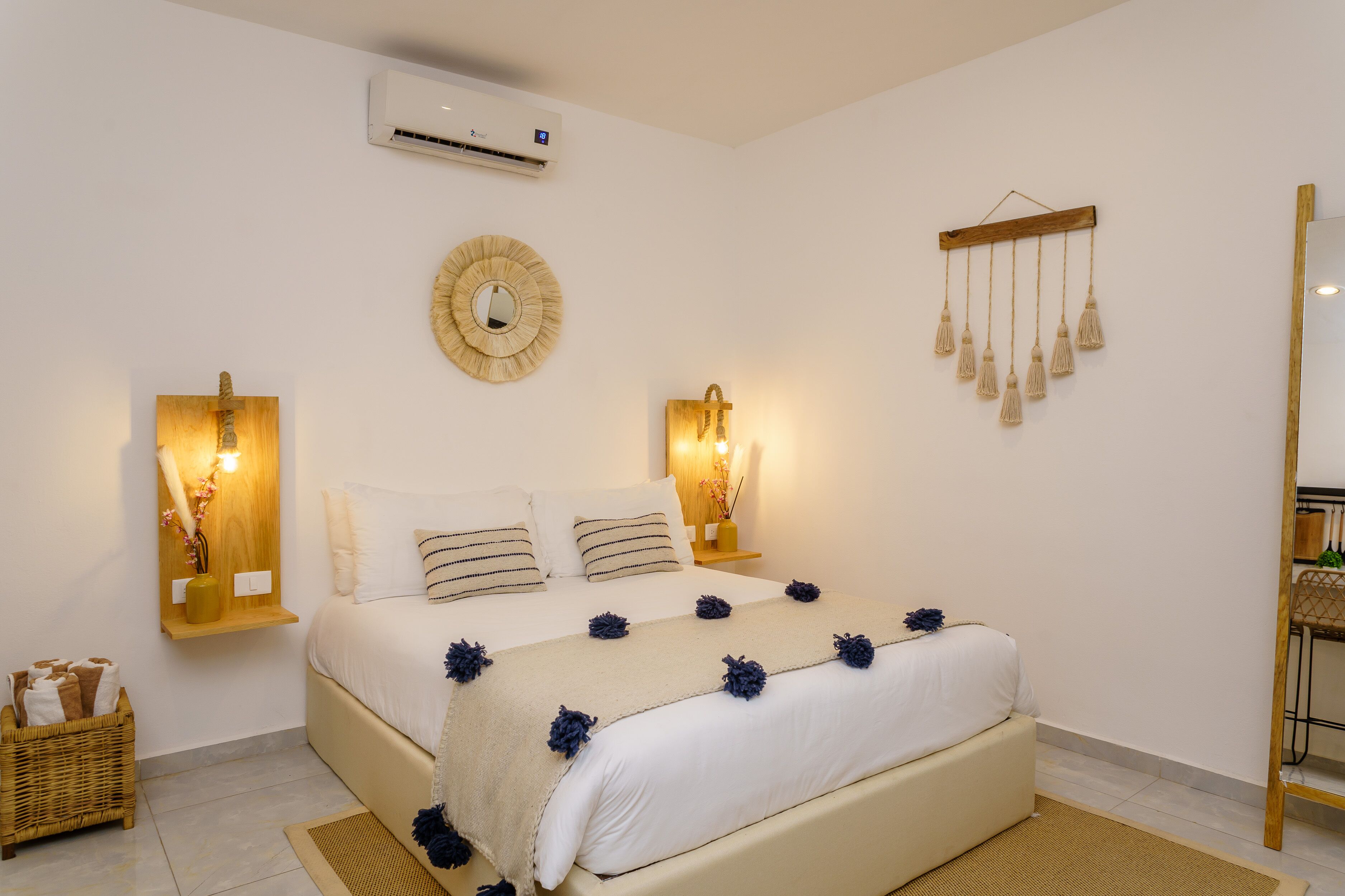 Un dormitorio ordenado con cama, lámparas de noche, aire acondicionado montado en la pared y una lámpara colgante decorativa.