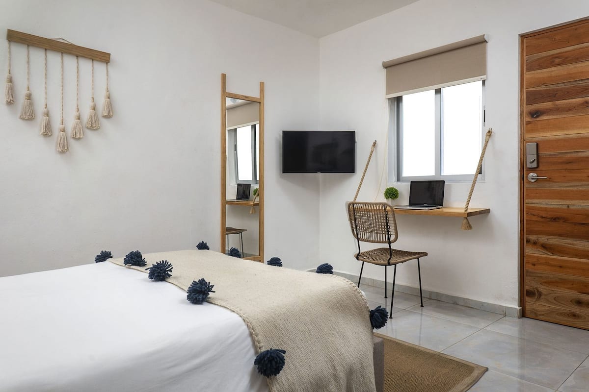 A bedroom with a bed, a desk with a chair, a TV, and a wooden door.