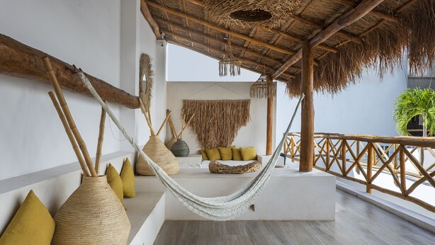 A hammock suspended between wooden beams, a white sofa with cushions, and a woven basket on a balcony with a railing. - Verandah Studios (Playa del Carmen)