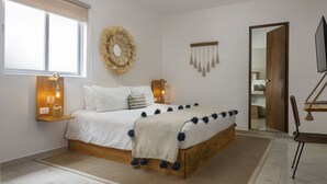 A bedroom with a wooden bed, a bedside table with a lamp, a wall-mounted mirror, and a large window. - Verandah Studios (Playa del Carmen)