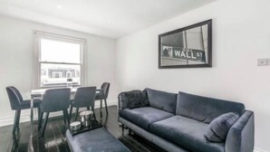 A modern living room with a grey sofa, black chairs, a coffee table, and a framed picture of Wall Street on the wall. - Flat close to Portobello Market (London)