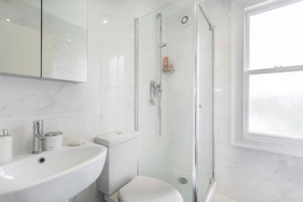 Uma casa de banho moderna com cabine de duche em vidro, lavatório branco e sanita.
