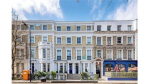 A row of terraced houses with a central entrance, a small garden, and a blue awning on the right. - Flat close to Portobello Market (London)