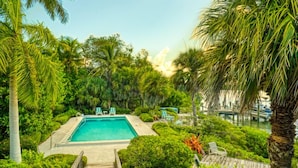 Una piscina rectangular rodeada de exuberante vegetación y palmeras, con una terraza de madera que conduce a la piscina.