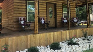 A log cabin with a porch, three folding chairs, and a door with a window.