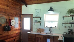 A rustic kitchen with wooden walls, a white countertop, a sink, and a window.
