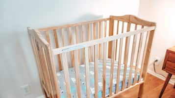 Una cuna de madera con una etiqueta de seguridad, ubicada en una habitación con suelo de madera y pared blanca.