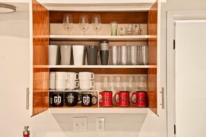 A cabinet with shelves containing various glassware and mugs. - Game Day Getaway: Pet-Friendly Razorback Stay (Fayetteville)
