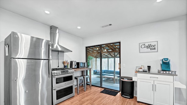 A modern kitchen with stainless steel appliances, a coffee bar, and a sliding glass door leading to an outdoor area.