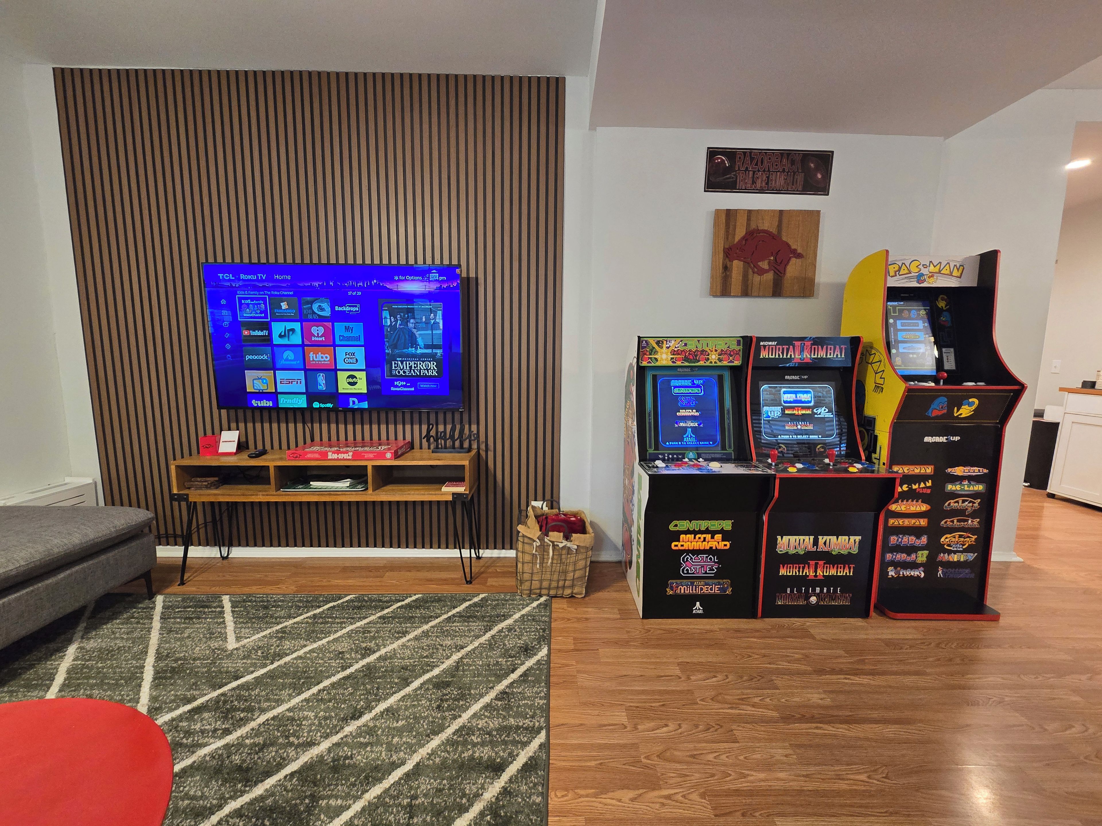 Ein Wohnzimmer mit Flachbildfernseher, einer Holzunterhaltungseinrichtung und Spielautomaten.