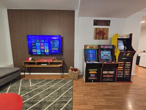 A living room with a flat-screen TV, a wooden entertainment unit, and arcade games.