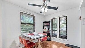 A room with a dining table, chairs, a ceiling fan, and a bookshelf.