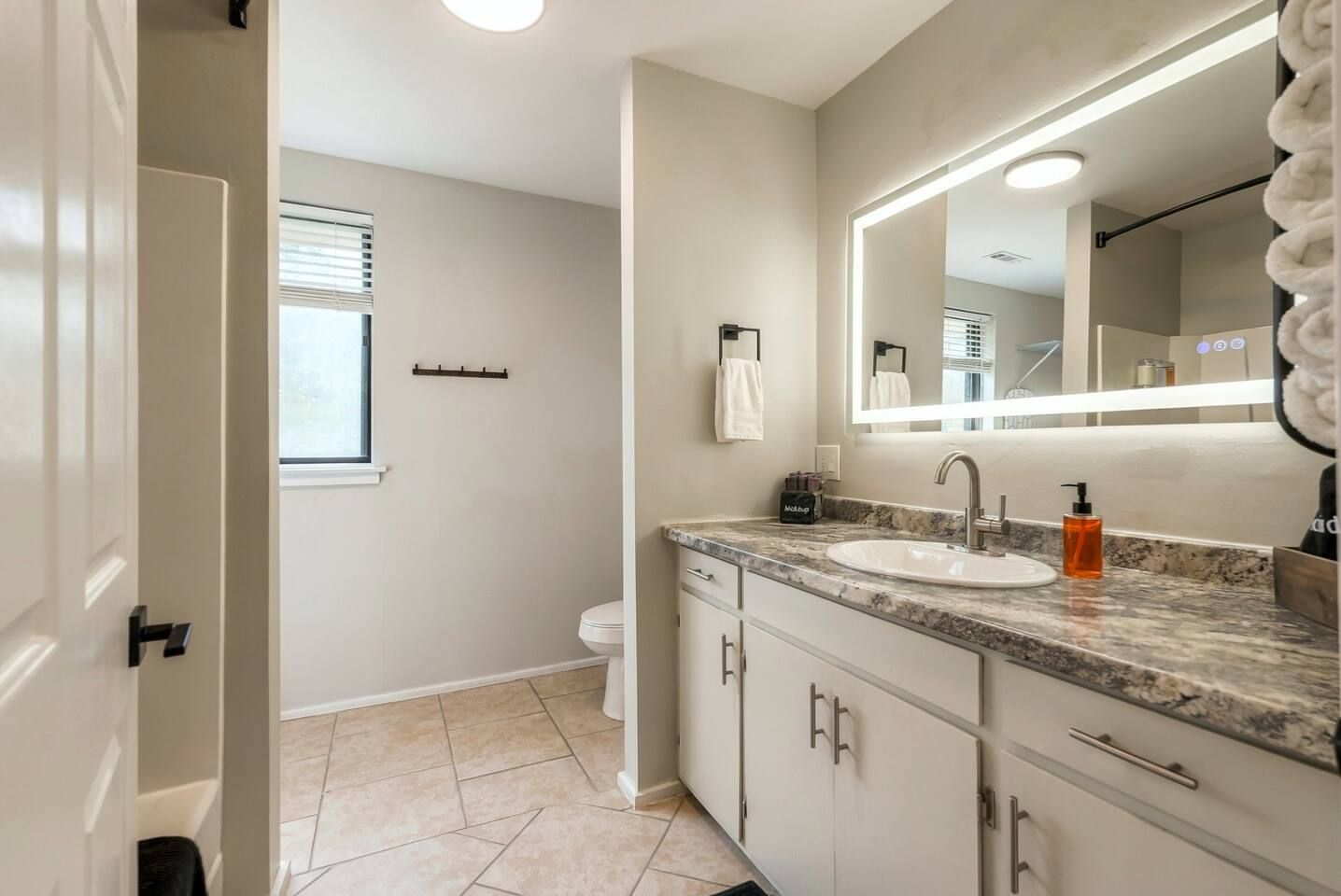 Full bathroom featuring a long vanity with LED illuminated mirror, spacious counter, and tile flooring.