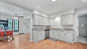 A modern kitchen with white cabinets, a dishwasher, and a dining area with red chairs.