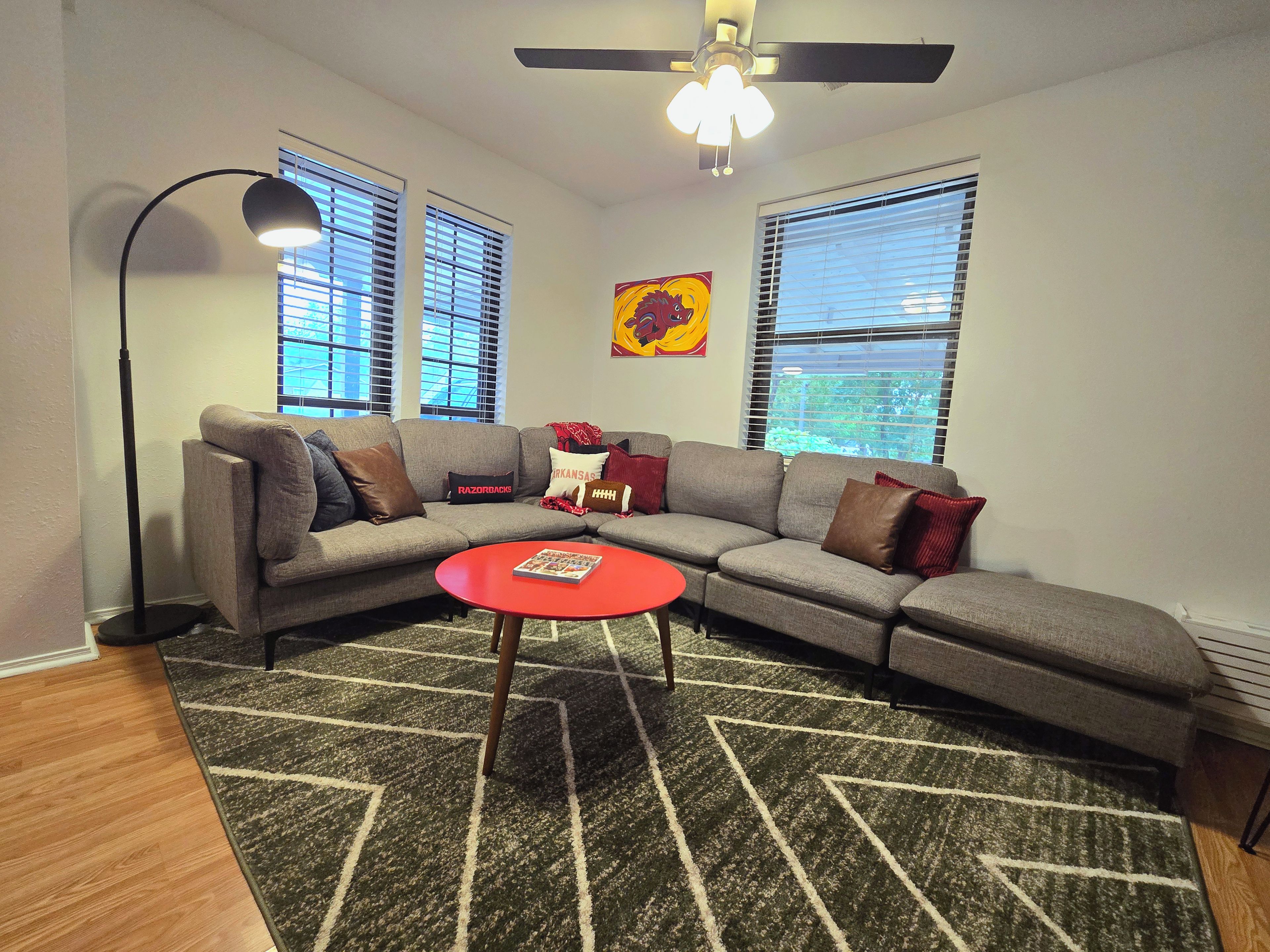 Ein Wohnzimmer mit einem Ecksofa, einem roten Couchtisch und einem gemusterten Teppich.