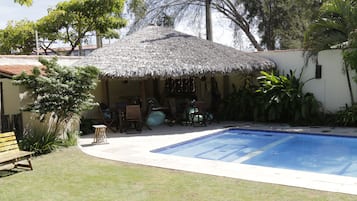 Un área de piscina con una estructura de techo de paja, un banco de madera y una pequeña mesa.