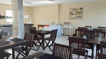 Un espace repas avec plusieurs tables et chaises, un coin cuisine équipé d’une cuisinière et d’étagères, et un mur orné d’un collage d’images.