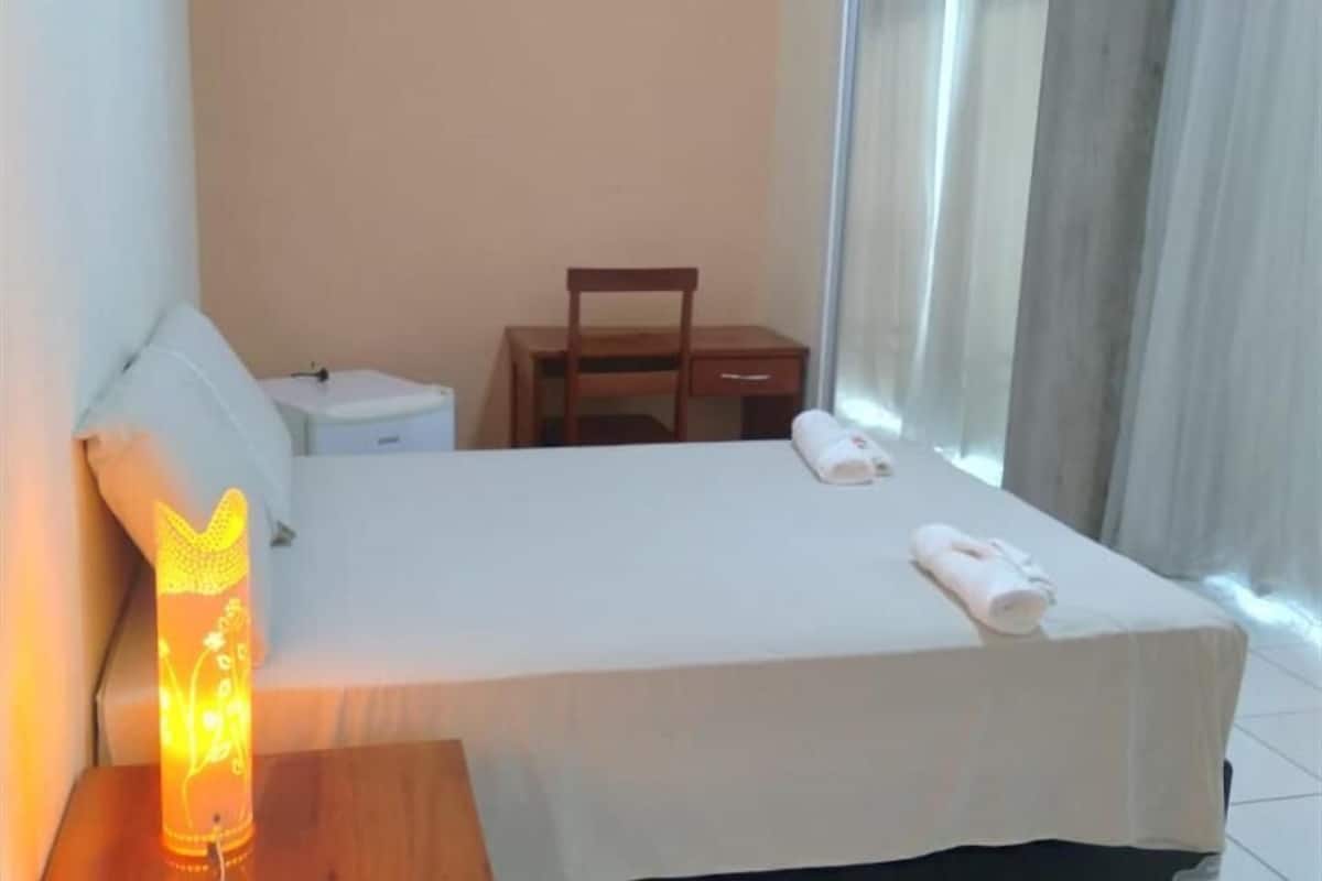 A hotel room with a bed, a nightstand, a chair, and a window with curtains.