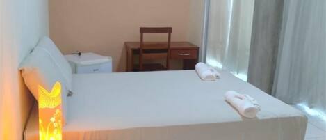 A hotel room with a bed, a nightstand, a chair, and a window with curtains.