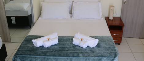 Una habitación de hotel con una cama, dos almohadas, una mesita de noche con lámpara y dos toallas sobre la cama.