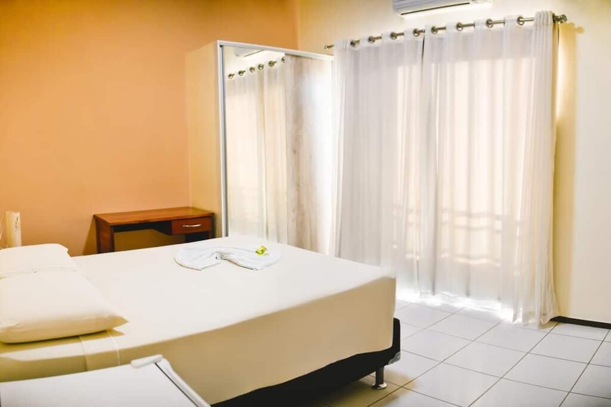 A hotel room with a bed, a bedside table, a chair, and a shower area.