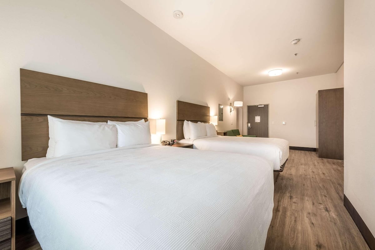 A hotel room with two beds, a wooden headboard, bedside lamps, a nightstand, and a door.