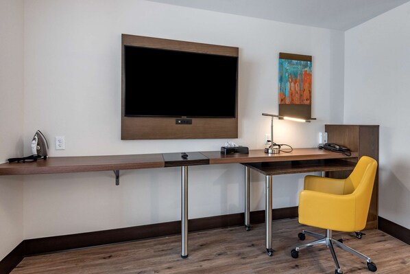 Una habitación de hotel moderna con un televisor de pantalla plana grande montado en la pared, un escritorio con una lámpara y una silla de oficina amarilla.