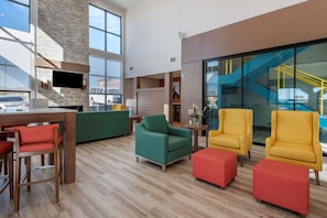 Un vestíbulo amplio con techo alto, una pared decorativa de piedra, un televisor de pantalla plana y una escalera con barandas amarillas.