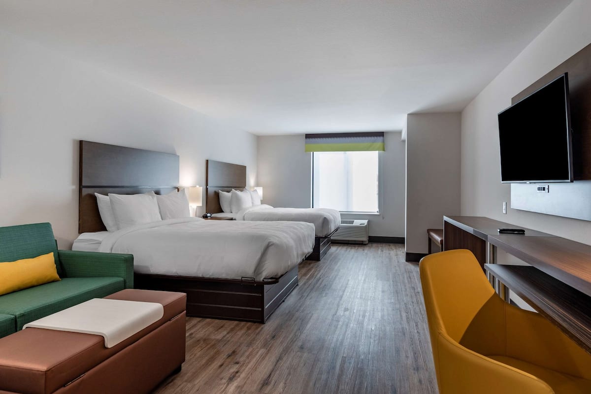 A hotel room with two beds, a sofa, a TV, and a desk.