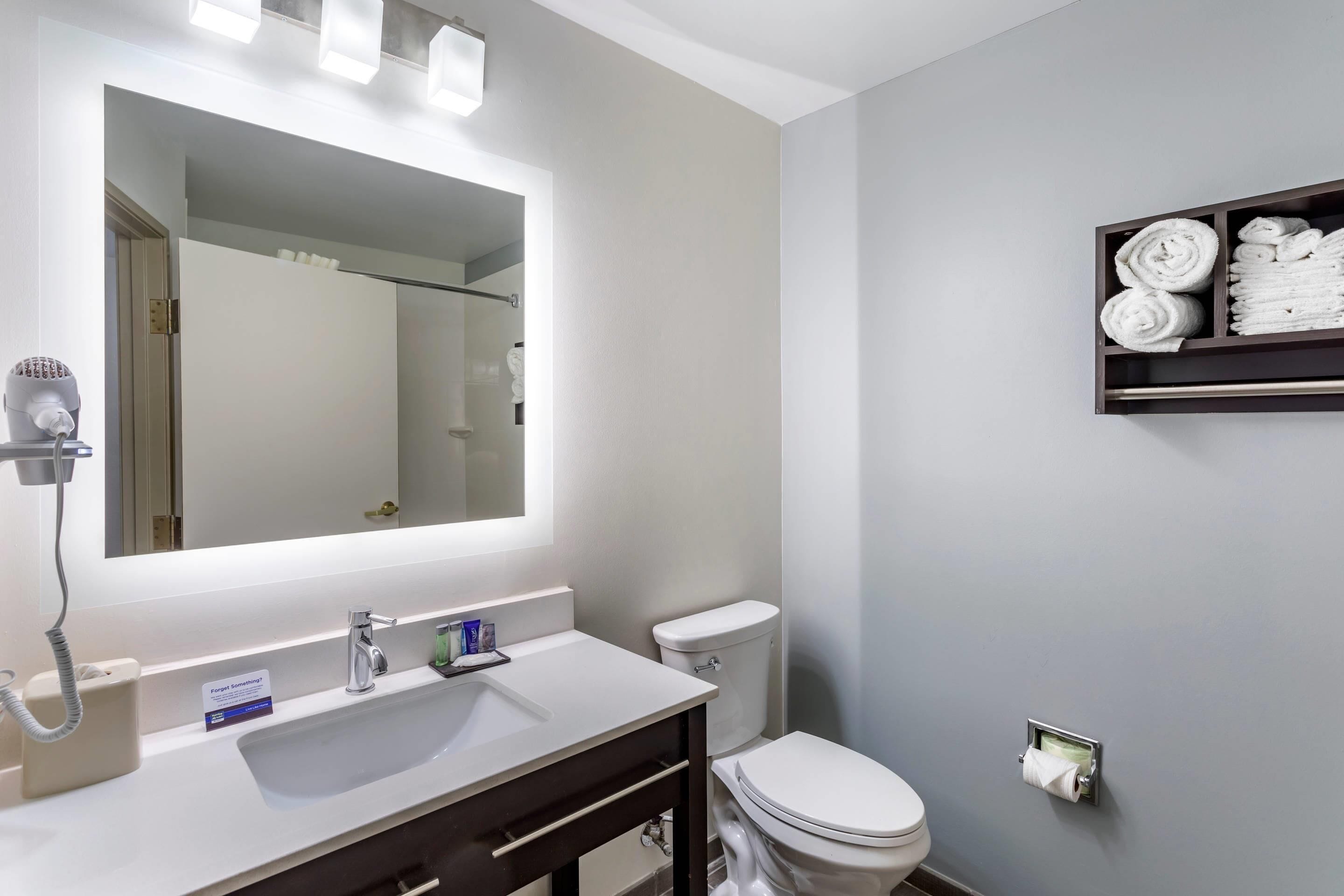 Een badkamer met een wastafel, spiegel, toilet, handdoekhouder en handdroger.
