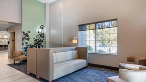 A modern lobby with a sofa, chairs, a patterned rug, a large window, and a wall with a floral design. - MainStay Suites Lebanon - Nashville Area (Lebanon)