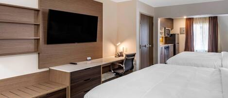 A hotel room with a bed, a desk with a chair, a TV mounted on the wall, and a kitchenette area.