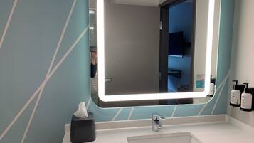 A bathroom with a large mirror, a sink, and a tissue box.